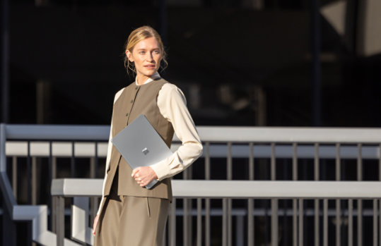 A person holds a 13.8-inch Surface Laptop for Business with 5G while crossing the street, suggesting the device’s secure design even in public settings.