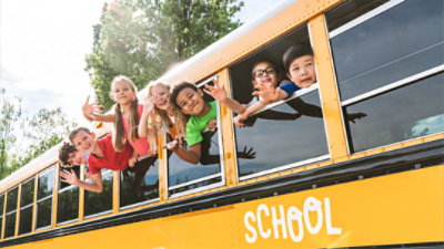 A group of primary school children waving out the windows of a school bus