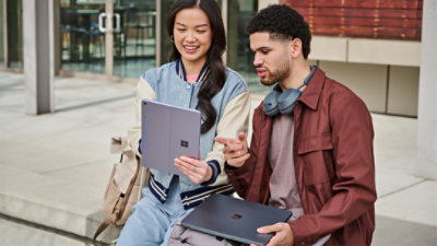 A woman showing a man her Surface Pro 2-in-1 outside of a building