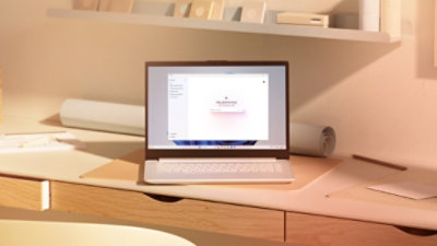 An open laptop with the Copilot app on the screen sitting on a desk with a chair, drawers, shelves and framed picture