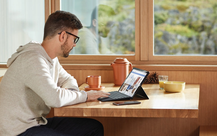 Person working with a PC in a casual setting on a desk next to a window.