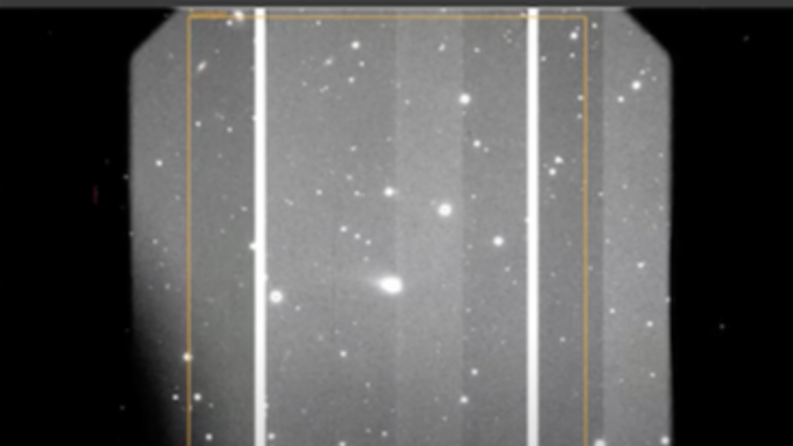 A gray scale image showing various white dots of stars and comets with a large smudge in the middle which is the interstellar comet 3I/ATLAS