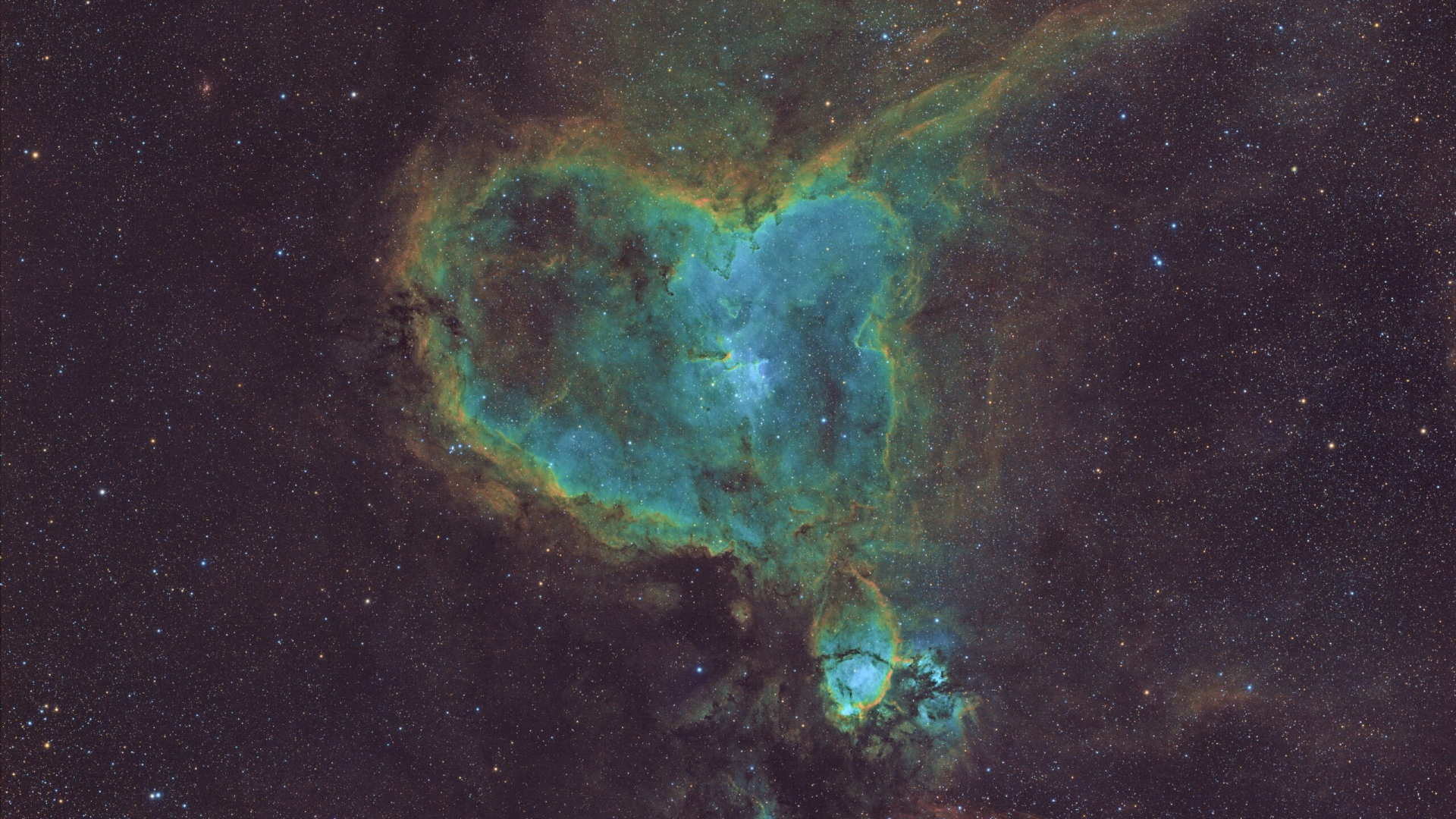 A swirling deep space nebula is pictured that takes the vague shape of a cartoonish human heart. The centre of the heart nebula is a pale blue/teal, while the outside is formed of dense dusty filaments of yellow and brown. A colorful starfield is visible in the background.