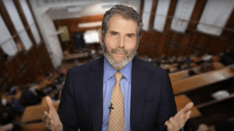 John Stossel stands in an auditorium | Stossel TV