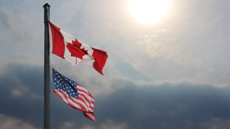 A flagpole with a Canadian flag on top and an American flag underneath, against a sunny sky. | Vergil Kanne | Dreamstime.com