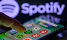 The Spotify app icon is being displayed on a smartphone with Spotify visible in the background.