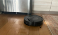 Roomba Combo robot vacuum mopping hardwood floor with refrigerator and rug in background