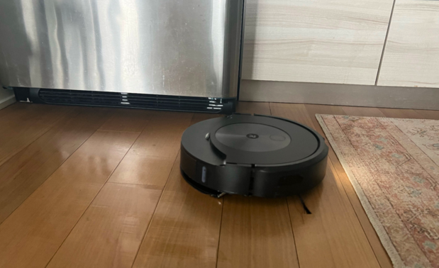 Roomba Combo robot vacuum mopping hardwood floor with refrigerator and rug in background