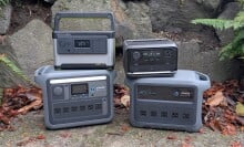 portable power stations from anker, goal zero, and ecoflow arranged together in front of a rockery with fall leaves on the ground