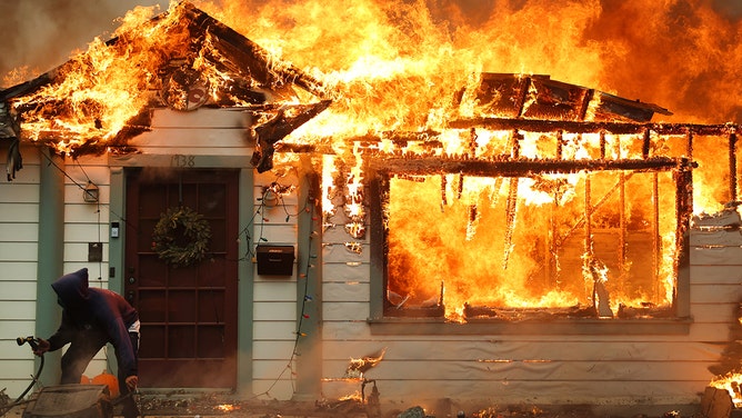 A person turns on a garden hose in an effort to save a neighboring home from catching fire during the Eaton Fire on January 8, 2025 in Altadena, California.