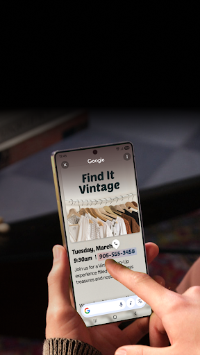 A person is holding a phone and circles the contact information for a vintage store. In the background is a table with stacked books and drumsticks on it.