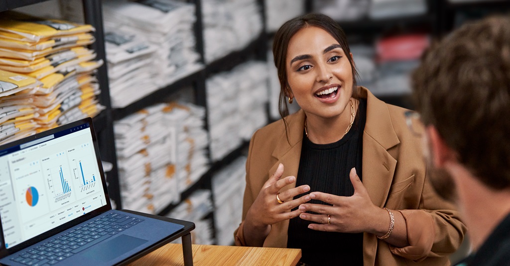 A businesswoman in a warehouse talking with a worker.