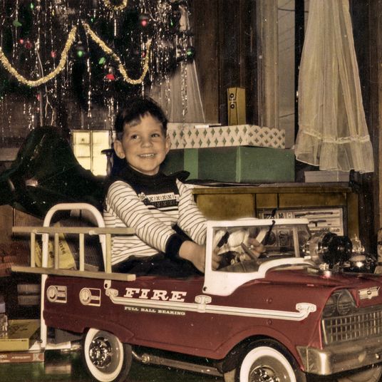 A little boy is in his new, toy fire engine Christmas morning.
