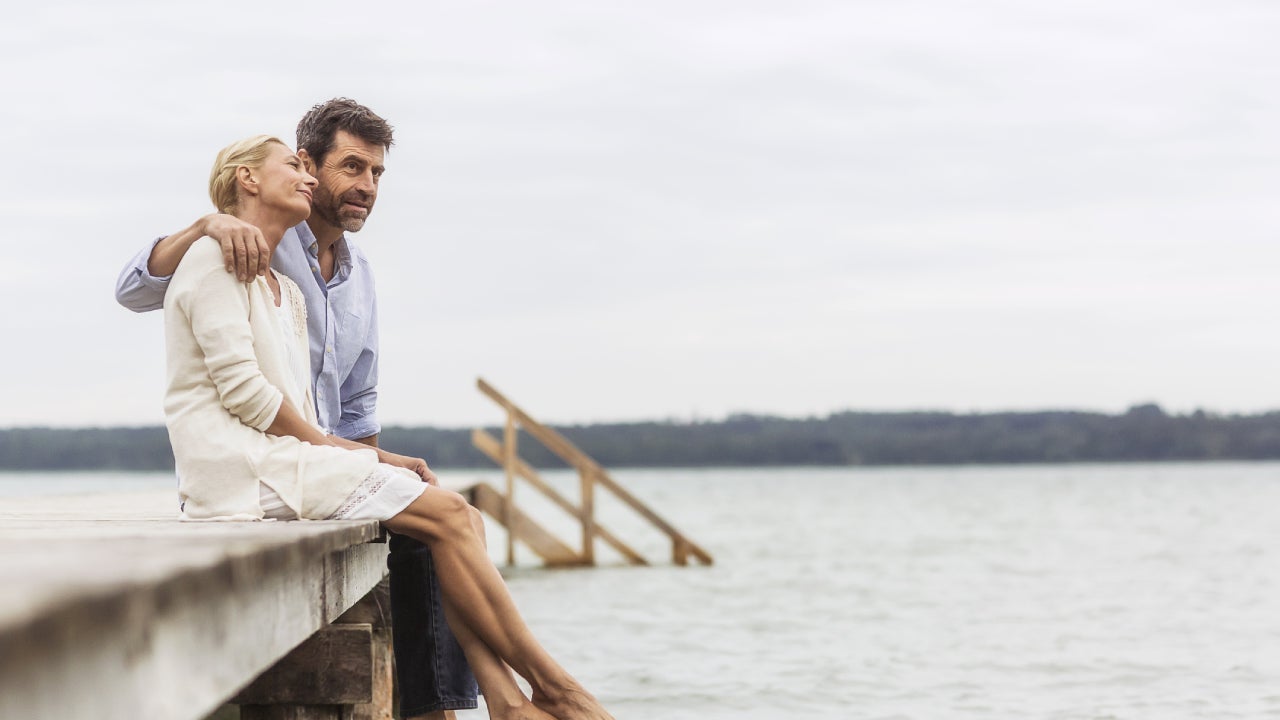 Older couple sitting together on a dock over a lake.