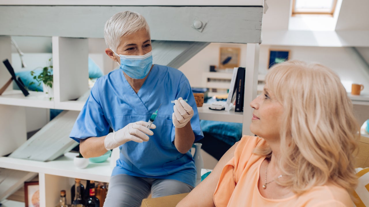 An older nurse drawing blood from a woman.