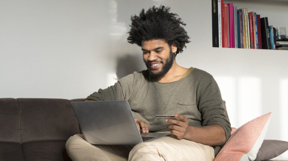 Man sitting on couch in living room with laptop and credit card