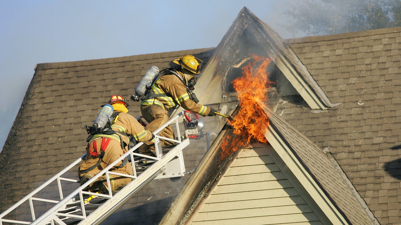 two firefighters on a ladder working to put out a house fire