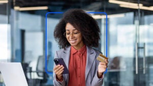 A young Black woman in a suit smiles at her phone.