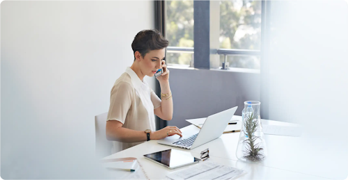 A professional at her desk multitasking on the phone in front of laptop.